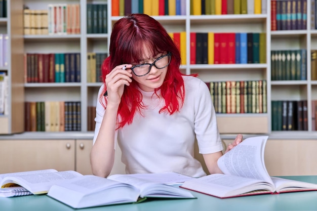 Tiener studenten studeren in de bibliotheek klas zitten aan het bureau met behulp van boeken schrijven in notebook Mode student met rood gekleurd haar dragen bril College studie onderwijs kennis adolescentie