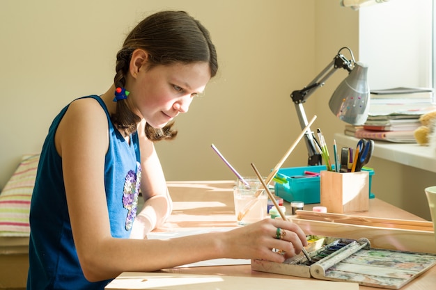 Tiener trekt aquarel aan een tafel in de kamer