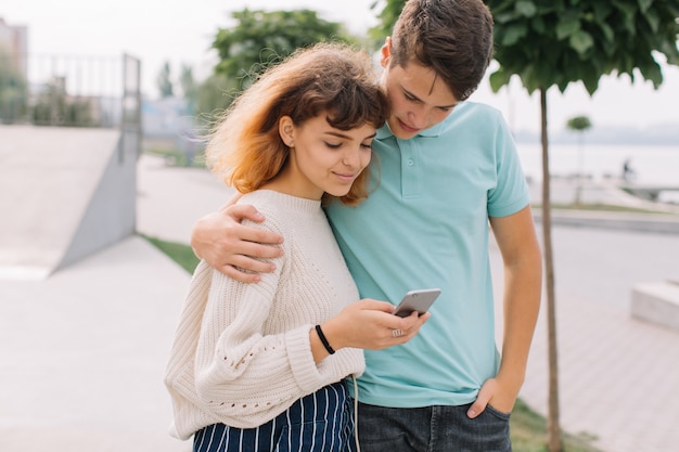 Tiener twee, jongen en meisje in het park en het gebruiken van smartphone.