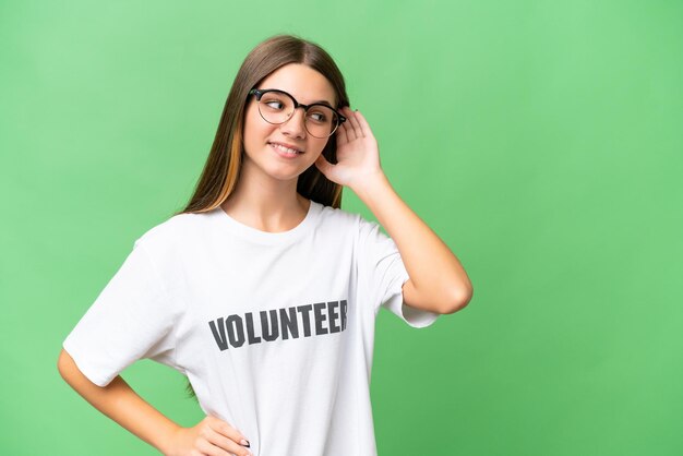 Tiener vrijwillig blank meisje over geïsoleerde achtergrond luisterend naar iets door hand op het oor te leggen