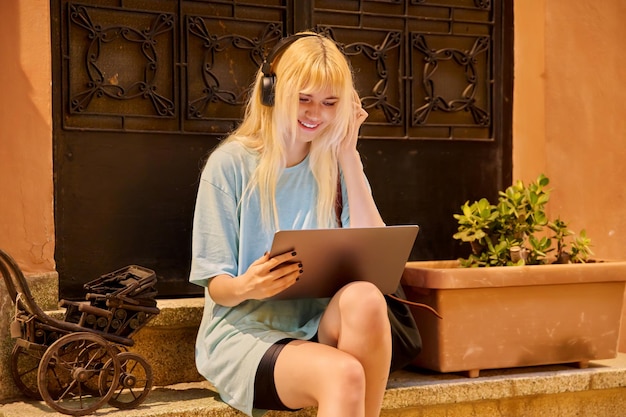 Tiener vrouwelijke student met behulp van laptop zittend op de trappen van het huis in de avond stad