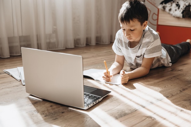 Tienerjongen die op vloer ligt met laptop met videogesprek en online les thuis schooljongen die huiswerk bestudeert afstandsonderwijs op afstand trainingsconcept