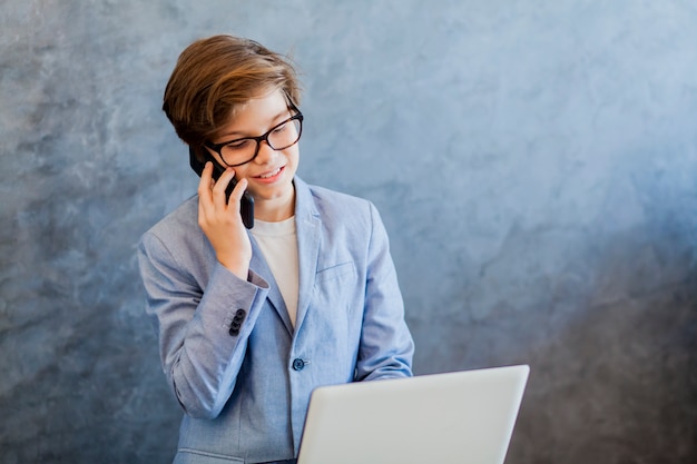 Tienerjongen die over mobiele telefoon spreekt en laptop met behulp van