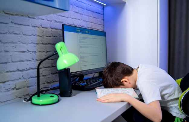 Tienerjongen die zelf op het bureau ligt. Een powernap doen tijdens het studeren en voorbereiden op huiswerk. Computer e-learning. Uitgeput en moe studentenconcept.