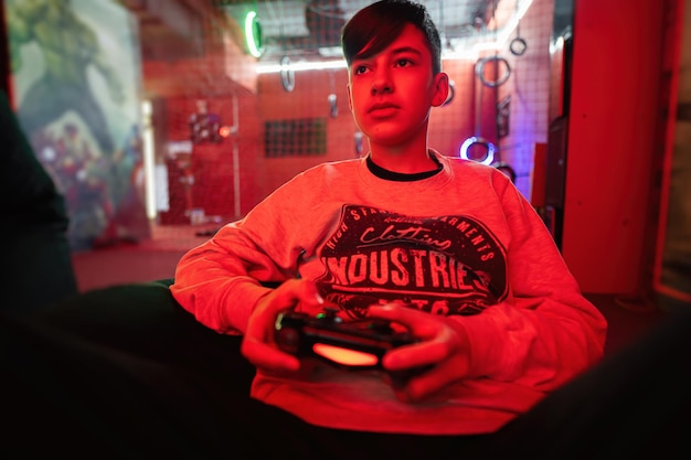 Foto tienerjongen gamer speelt gamepad-videogameconsole in rode speelkamer
