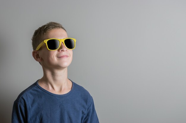 Tienerjongen in zonnebril en blauwe t-shirt op lichte achtergrond