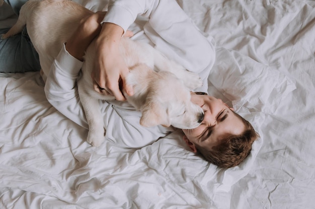 Tienerjongen ligt in bed op wit beddengoed met hond bovenaanzicht huisdier maakt de eigenaar 's ochtends wakker