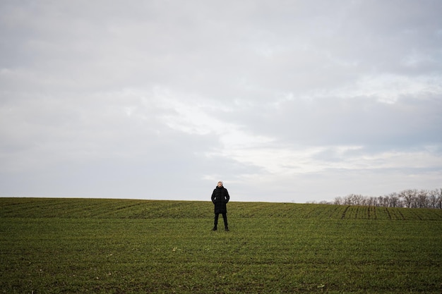 Tienerjongen met zwarte jas en witte hoed buiten geniet van in het vroege voorjaarsveld