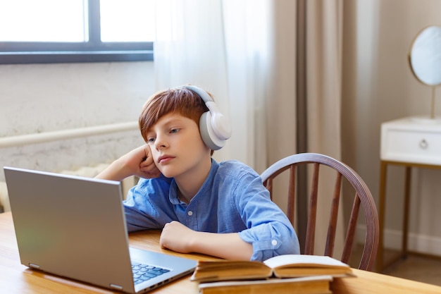 Tienerjongen tijdens een online les zit hij in een koptelefoon en luistert naar een saai lesonderwerp