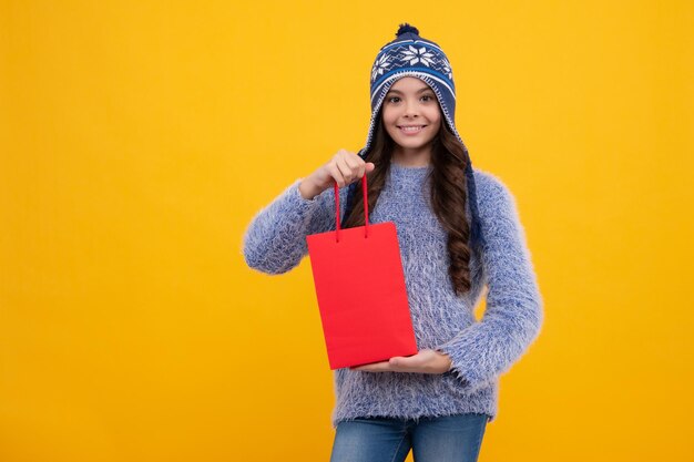 Tienerkindmeisje in de herfsthoed met boodschappentassen op gele achtergrond Kid with shopping winter