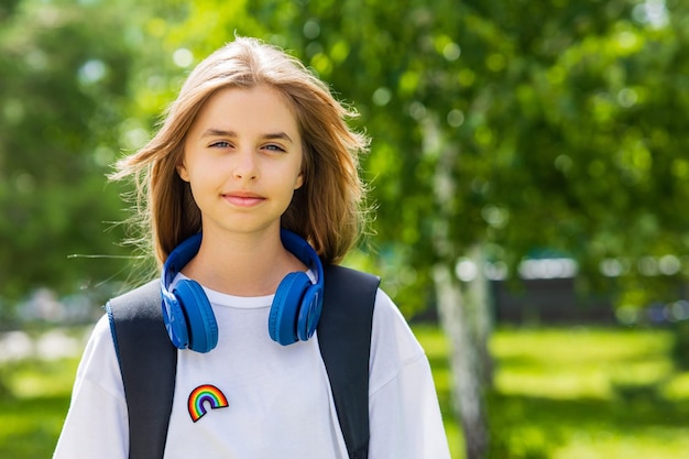 Tienerleeftijdsmeisje met rugzak en hoofdtelefoon in park terug naar schoolconcept