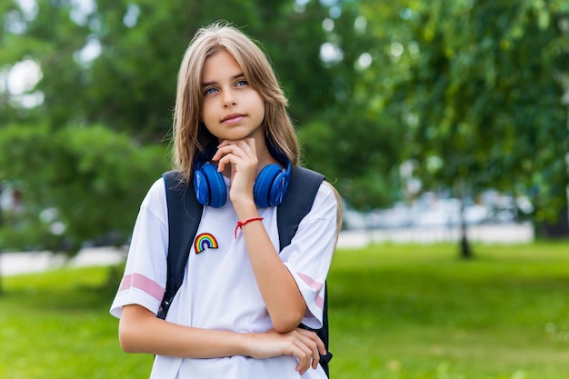 Tienerleeftijdsmeisje met rugzak en hoofdtelefoon in park terug naar schoolconcept