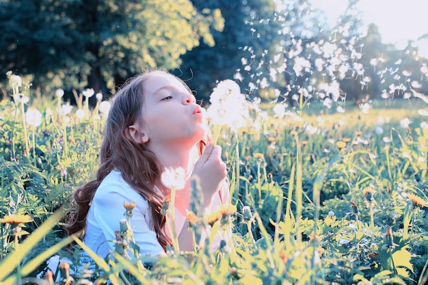 Tienermeisje blaast zaden van een bloempaardebloem in een lentepark