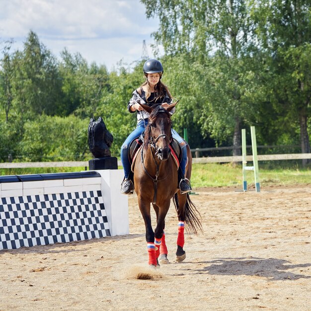 Tienermeisje dat een helm draagt, leert op een paard te rijden op het paardrijveld