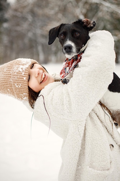 Tienermeisje dat in het winterpark staat en een zwarte hond vasthoudt