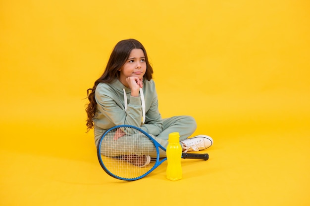 Tienermeisje dat water gaat drinken na sporttraining. badmintonspeler ontspannen. gezonde en actieve levensstijl. jeugd. gehydrateerd zijn. triest kind zit met racket en waterfles. kind met tennisracket.