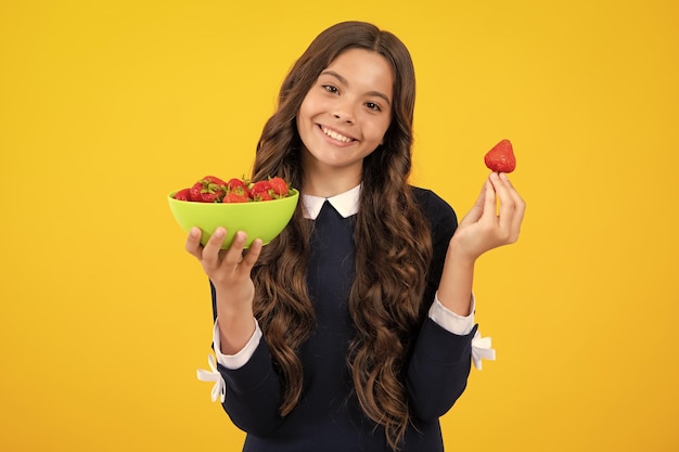 Tienermeisje die een aardbeikind met aardbeikom op gele achtergrond proeft Biologische aardbeien