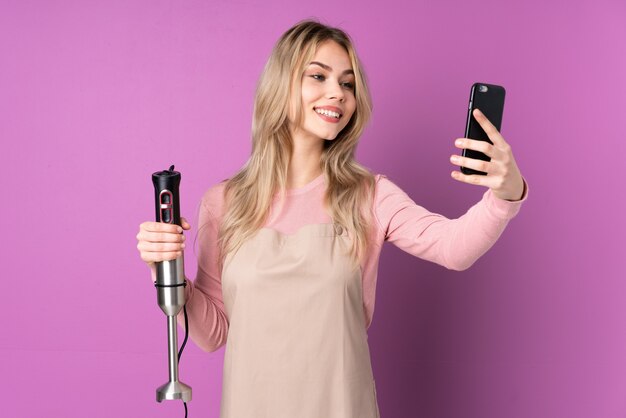 Tienermeisje die geïsoleerde handmixer gebruiken het maken van een selfie