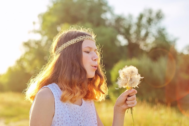 Tienermeisje die met hippiekapsel op droge paardebloemen blazen. Zomervakantie, vakantie, natuur, schoonheid, levensstijl. Hemel, weide, zonsondergang verlichting achtergrond