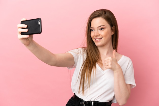 Tienermeisje die over geïsoleerde roze achtergrond een selfie met mobiele telefoon maken