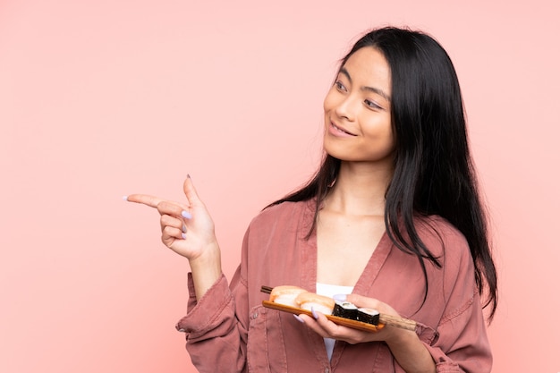 Tienermeisje die sushi eten die op roze wijzende vinger aan de kant wordt geïsoleerd