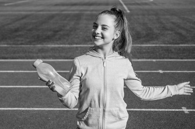 Tienermeisje drinkt water tijdens het trainen en rennen in het buitenstadion, dorstig