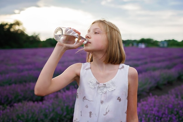 Tienermeisje drinkt zuiver water uit glazen fles bij Lavendel veld hittegolf zomer reizen