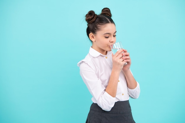 Tienermeisje drinkwater uit glas op blauwe achtergrond Dagelijks leven gezondheid Drink water voor gezondheidszorg en lichaamsbalans Dorst kind uitdroging