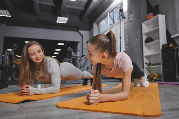 Tienermeisje geniet van trainen in de sportschool met persoonlijke trainer die plankoefening doet