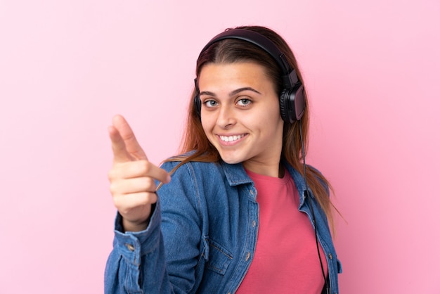 Tienermeisje het luisteren muziek over geïsoleerde roze muur