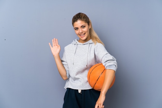 Tienermeisje het spelen basketbal het groeten met hand met gelukkige uitdrukking