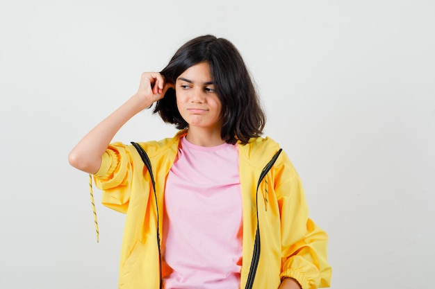 Tienermeisje houdt hand op oren in geel trainingspak, t-shirt en kijkt peinzend, vooraanzicht.
