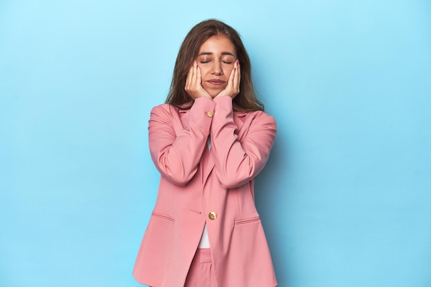 Tienermeisje in chique roze pak op een blauwe achtergrond troosteloos zeurend en huilend