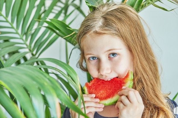 Tienermeisje in een blauwe jurk met stippen die een watermeloen eten.