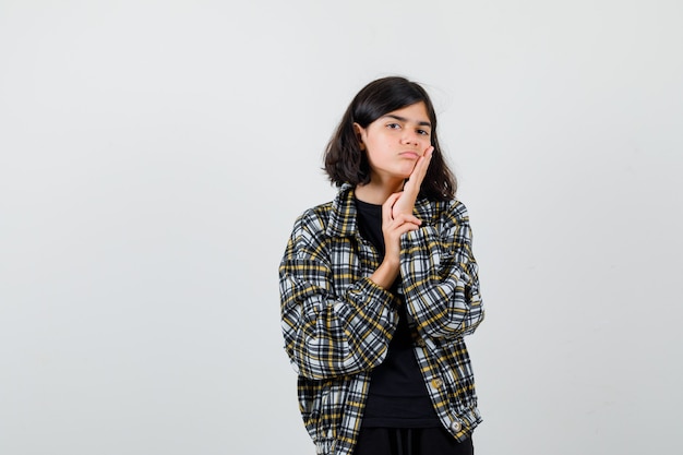 Tienermeisje in een casual shirt dat de hand op de wang houdt en er somber uitziet, vooraanzicht.