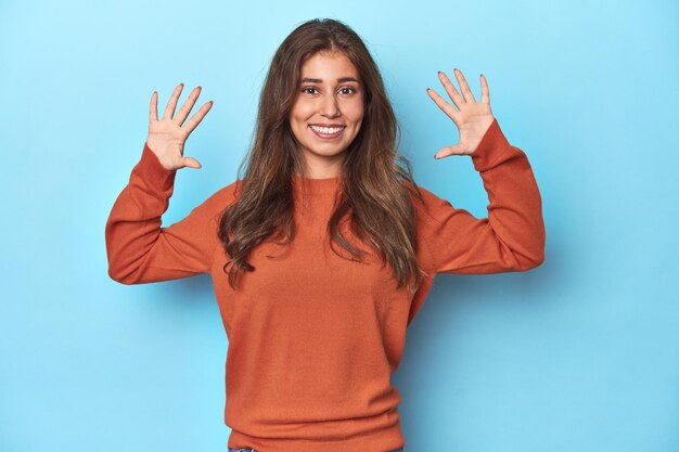 Foto tienermeisje in een levendige oranje trui op blauw met nummer tien met handen