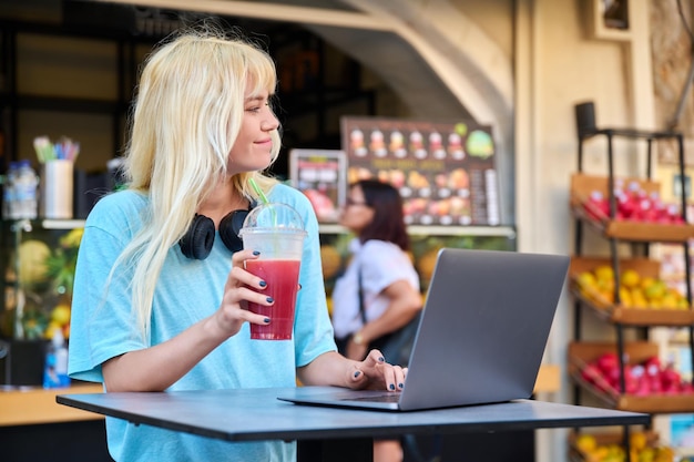 Tienermeisje in fruit buiten fruitsap bar drinken vitamine vers sap met behulp van laptop