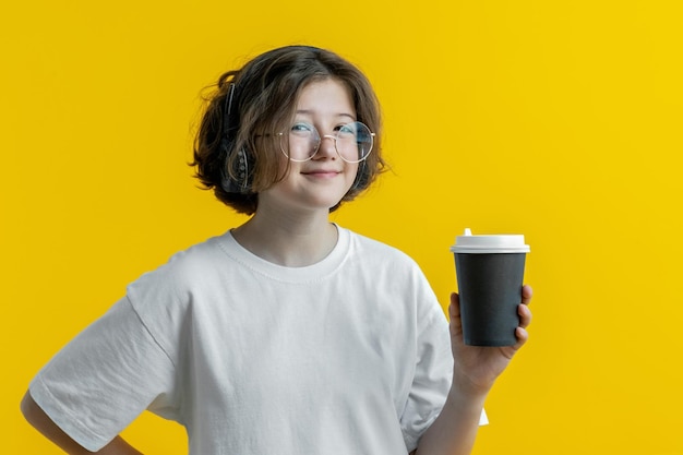 Tienermeisje in glazen koptelefoon met kopje koffie op gele achtergrond
