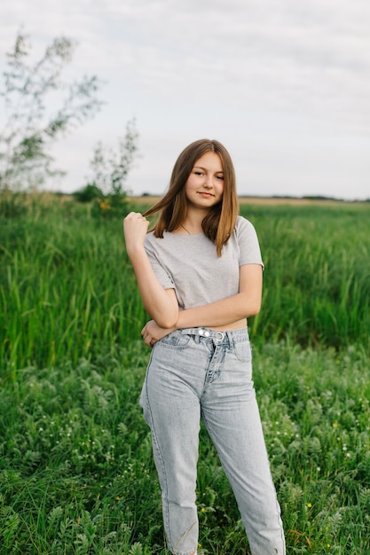 tienermeisje in grijze t-shirts en grijze spijkerbroek op het groene gras Natuurwandeling in zomervakantie