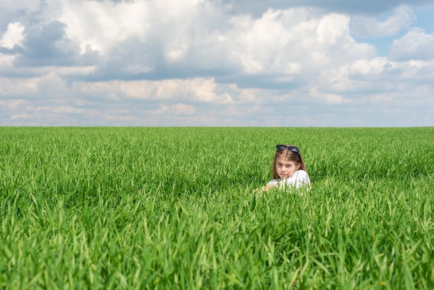 Tienermeisje in groen gras in het veld tegen de achtergrond van een bewolkte hemel