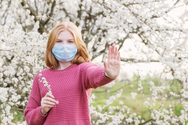 Tienermeisje in medisch masker in de lente bloeiende tuin. Concept van sociale afstand en preventie van coronavirus.