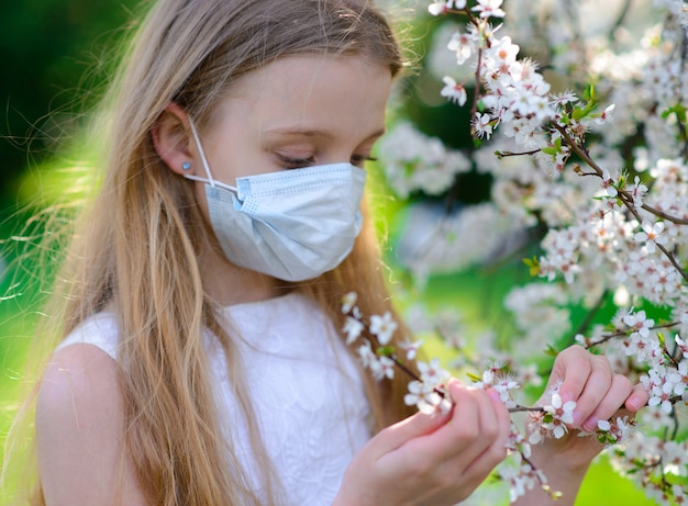 Tienermeisje in medisch masker in de lente bloeiende tuin