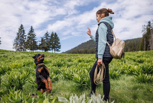 Tienermeisje in pak staat en geeft commando's aan hond van Rottweiler-ras op weide met vegetatie
