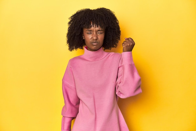 Tienermeisje in roze sweatshirt gele studio achtergrond toont vuist naar camera agressief