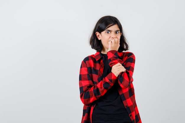 Tienermeisje in t-shirt, geruit hemd dat op haar nagels bijt en er angstig uitziet, vooraanzicht.