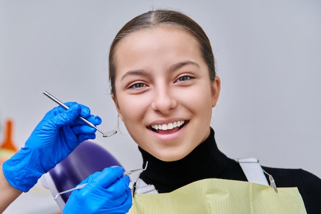 Tienermeisje in tandartsstoel met handen van tandarts met gereedschap