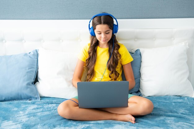 Tienermeisje kind in koptelefoon ontspannen op bed thuis luisteren naar muziek met laptop Kind in koptelefoon surfen op internet op computer