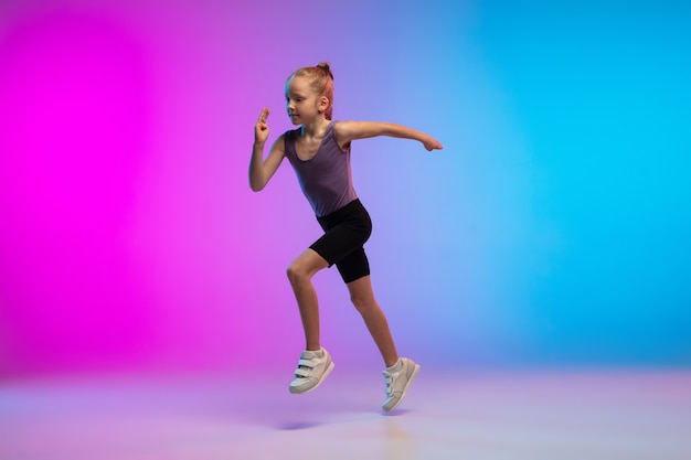 Tienermeisje loopt joggen tegen gradiënt roze blauwe neon studio achtergrond in beweging