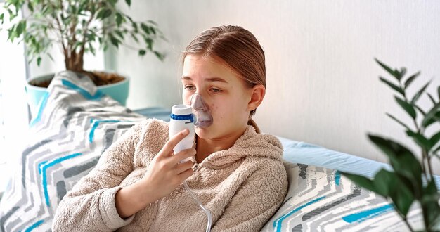 Tienermeisje maakt inademing met een vernevelaar-apparatuur. ziek kind houdt inhalator in de hand en ademt thuis door een inhalator
