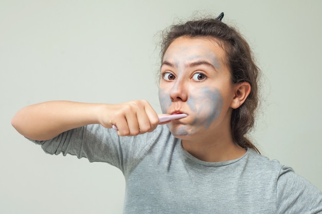 tienermeisje met een cosmetisch masker op haar gezicht poetst haar tanden. Facial scrub masker.